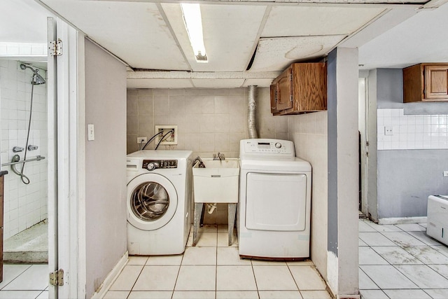 laundry area featuring cabinets, washer and clothes dryer, sink, light tile patterned floors, and tile walls