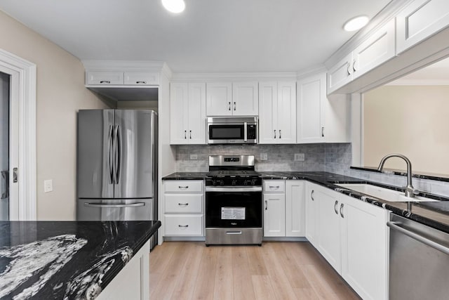 kitchen with appliances with stainless steel finishes, light wood-style floors, white cabinets, a sink, and dark stone counters