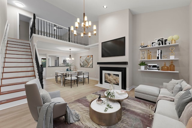 living area featuring baseboards, light wood-style flooring, a fireplace with flush hearth, stairway, and an inviting chandelier