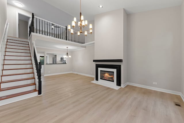 unfurnished living room featuring a chandelier, light wood finished floors, a fireplace with flush hearth, and a towering ceiling