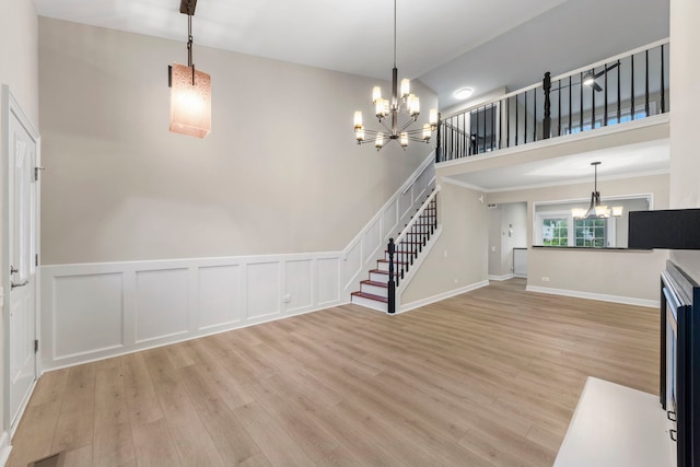 unfurnished living room with stairway, light wood finished floors, and an inviting chandelier