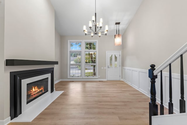 entrance foyer featuring a glass covered fireplace, a wainscoted wall, stairway, light wood-type flooring, and a decorative wall