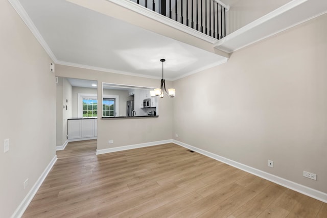 empty room with an inviting chandelier, light wood-style flooring, baseboards, and crown molding