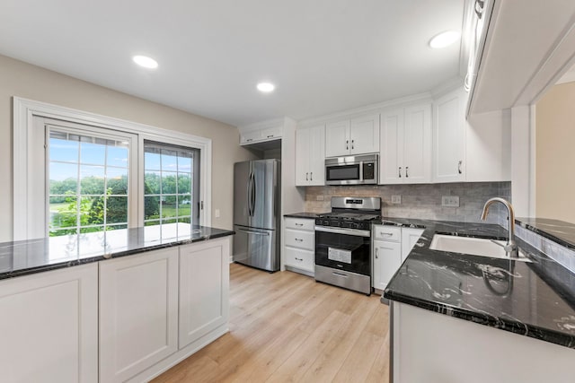 kitchen featuring appliances with stainless steel finishes, white cabinetry, a sink, light wood-type flooring, and dark stone counters