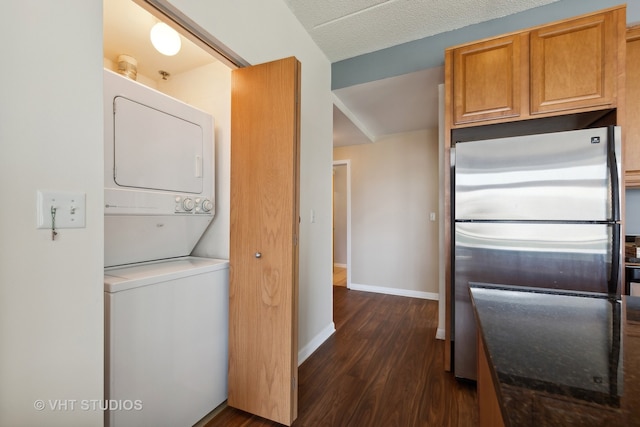 kitchen featuring dark wood-type flooring, stainless steel fridge, stacked washer and dryer, and a textured ceiling