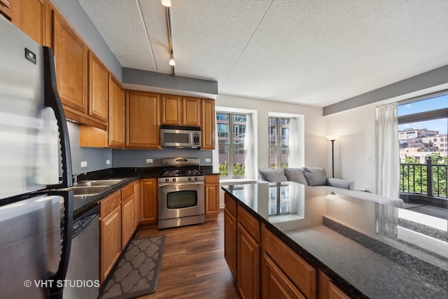 kitchen featuring a textured ceiling, dark wood-type flooring, appliances with stainless steel finishes, rail lighting, and sink