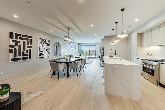 kitchen with hanging light fixtures, a center island with sink, high end stainless steel range, and sink