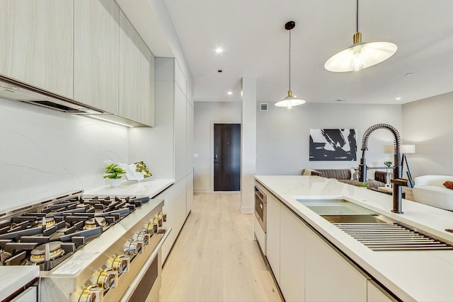 kitchen with sink, light hardwood / wood-style flooring, light stone countertops, stainless steel range, and decorative light fixtures