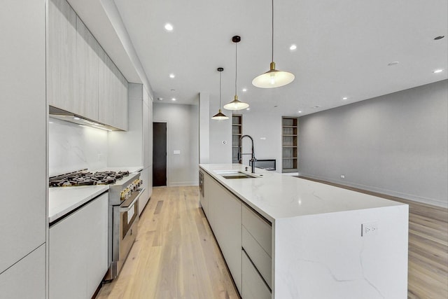 kitchen featuring sink, light hardwood / wood-style flooring, high end range, hanging light fixtures, and a large island with sink