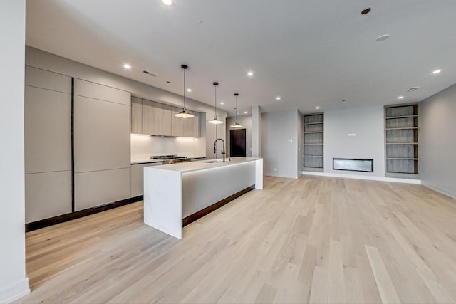 kitchen featuring pendant lighting, sink, built in features, light hardwood / wood-style floors, and an island with sink