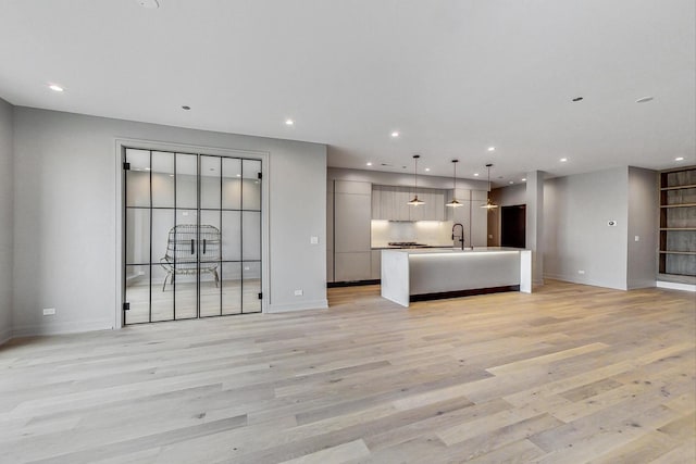 kitchen featuring a kitchen island with sink, hanging light fixtures, sink, and light wood-type flooring