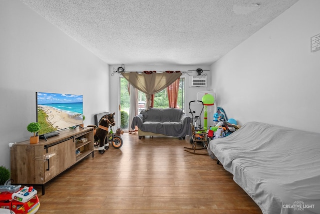 living room featuring a wall mounted AC, a textured ceiling, and hardwood / wood-style flooring