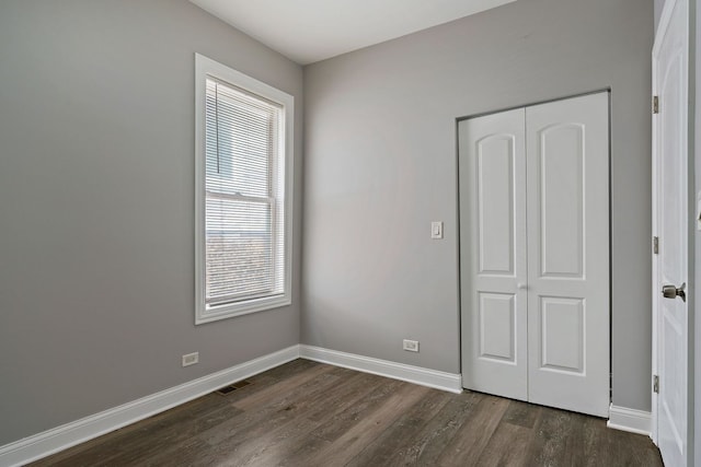 unfurnished bedroom featuring a closet, dark wood finished floors, visible vents, and baseboards