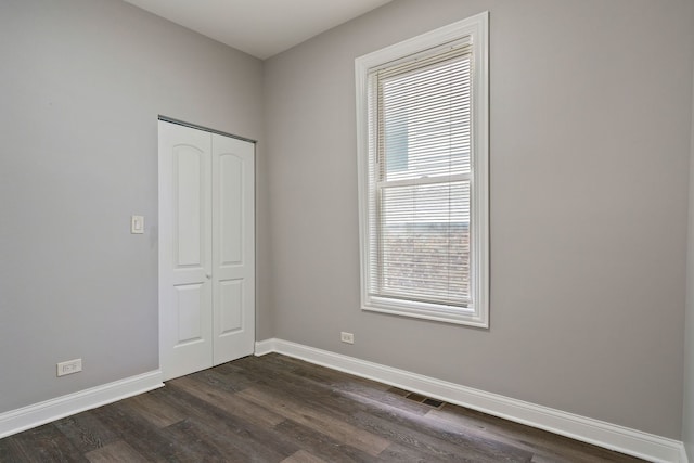 unfurnished room with dark wood-type flooring, visible vents, and baseboards