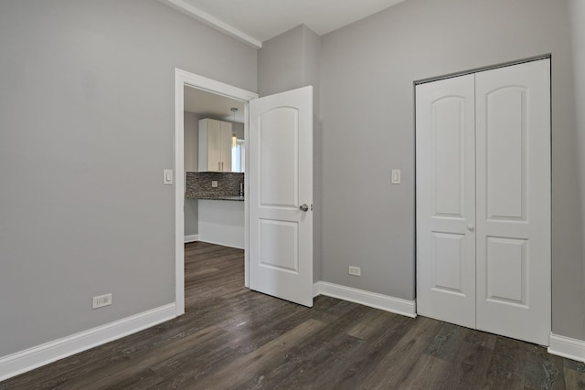 unfurnished bedroom featuring baseboards, dark wood finished floors, and a closet