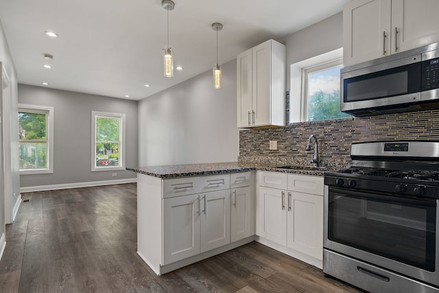 kitchen with white cabinets, appliances with stainless steel finishes, backsplash, a peninsula, and a sink