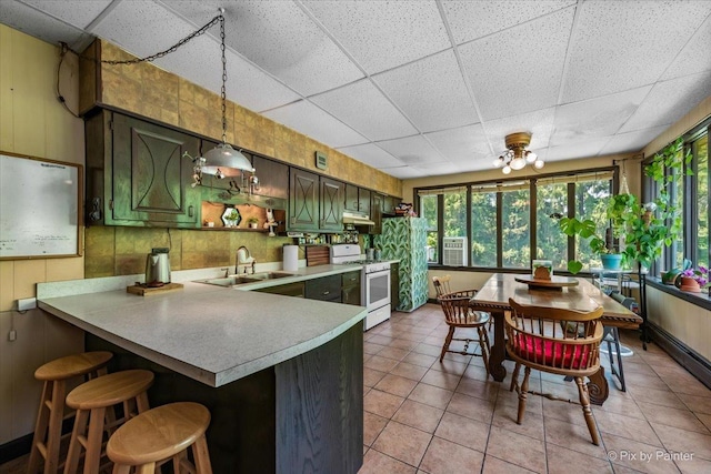 kitchen with a peninsula, white gas stove, a drop ceiling, a sink, and light countertops