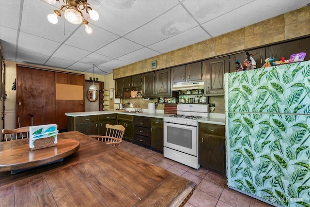 kitchen featuring white range with gas cooktop, a sink, light countertops, a paneled ceiling, and under cabinet range hood