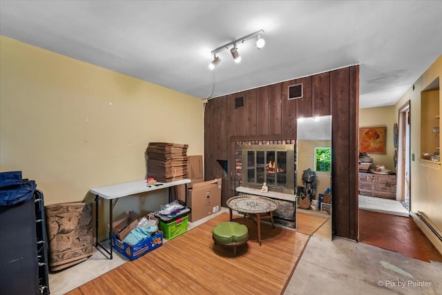 living room with a glass covered fireplace, wooden walls, wood finished floors, visible vents, and a baseboard heating unit