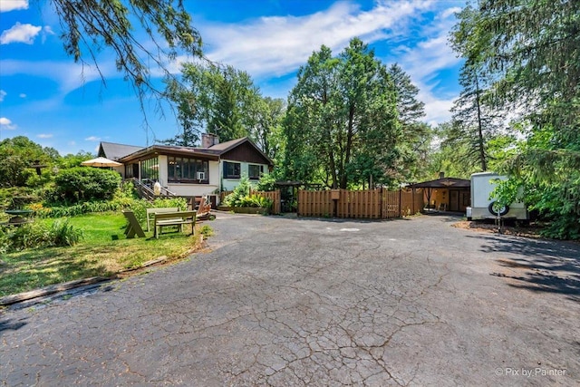 view of front of house featuring aphalt driveway, a chimney, and fence