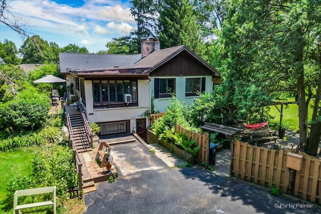 view of front facade featuring fence, aphalt driveway, stairway, stucco siding, and a chimney