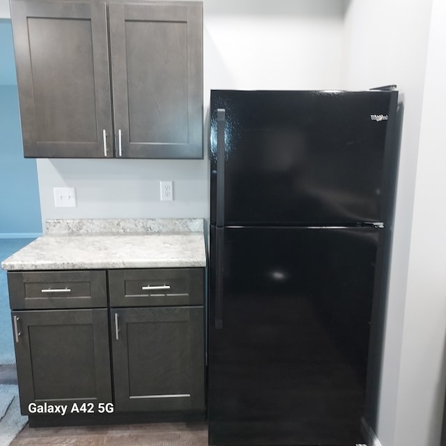 kitchen featuring baseboards, light stone counters, and freestanding refrigerator