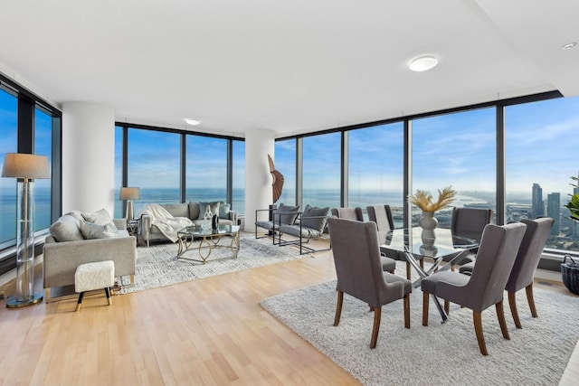 dining space with a water view, light hardwood / wood-style flooring, a wall of windows, and plenty of natural light