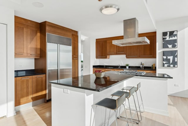 kitchen with a kitchen breakfast bar, a kitchen island, stainless steel appliances, and range hood