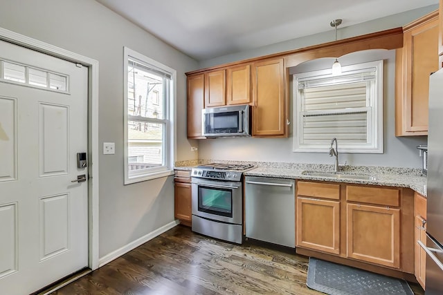 kitchen featuring sink, light stone countertops, hanging light fixtures, dark hardwood / wood-style floors, and appliances with stainless steel finishes