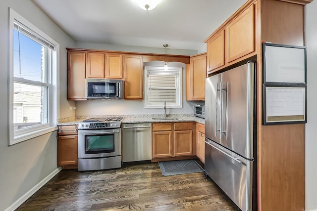 kitchen featuring dark hardwood / wood-style floors, light stone countertops, pendant lighting, appliances with stainless steel finishes, and sink