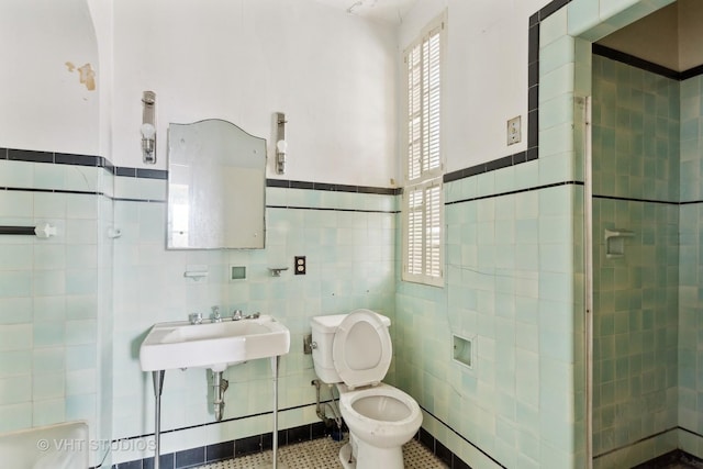 bathroom with sink, tile patterned flooring, tiled shower, toilet, and tile walls