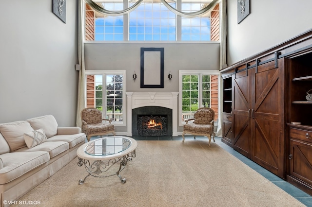 living room with a towering ceiling, a premium fireplace, a barn door, and carpet flooring