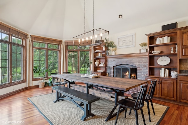 dining area featuring a fireplace, wood-type flooring, a wealth of natural light, and an inviting chandelier