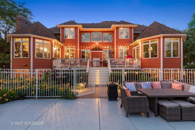 back house at dusk with an outdoor living space and a deck