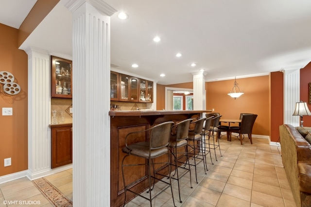 bar featuring tasteful backsplash, light tile patterned floors, decorative light fixtures, and ornate columns