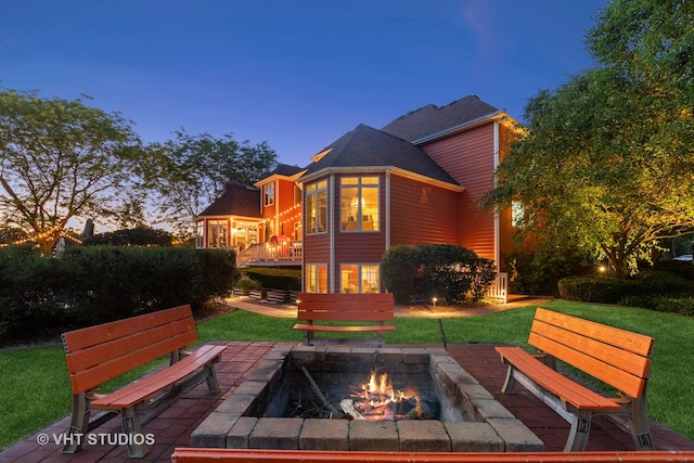 back house at dusk with a yard, a wooden deck, and an outdoor fire pit