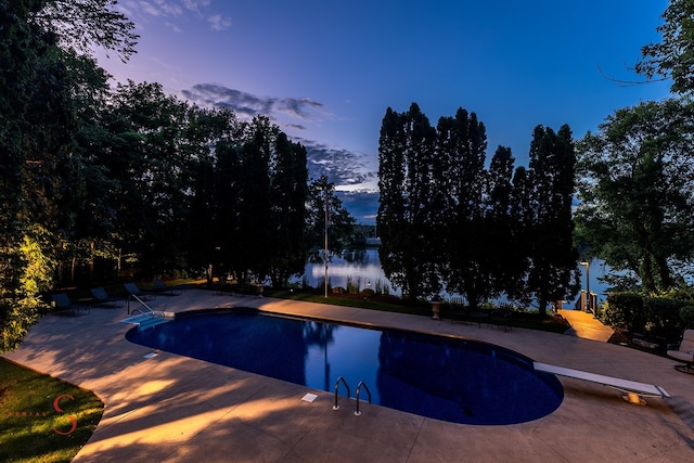 pool at dusk featuring a diving board and a patio area