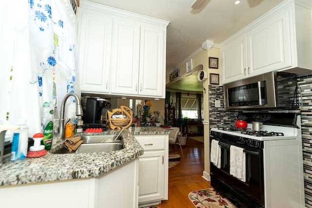 kitchen with white gas range oven, wood-type flooring, white cabinetry, and tasteful backsplash