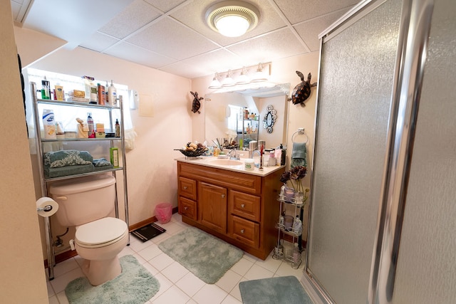 bathroom with a paneled ceiling, tile floors, a shower with door, vanity, and toilet