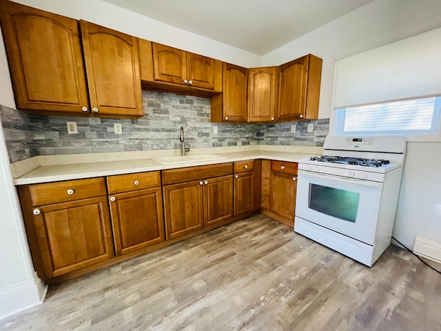 kitchen featuring white range with gas stovetop, sink, light wood-type flooring, and backsplash