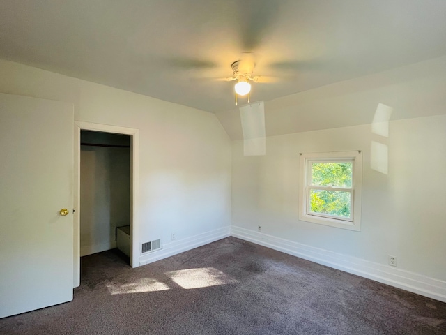 unfurnished bedroom featuring dark colored carpet, a closet, vaulted ceiling, and ceiling fan