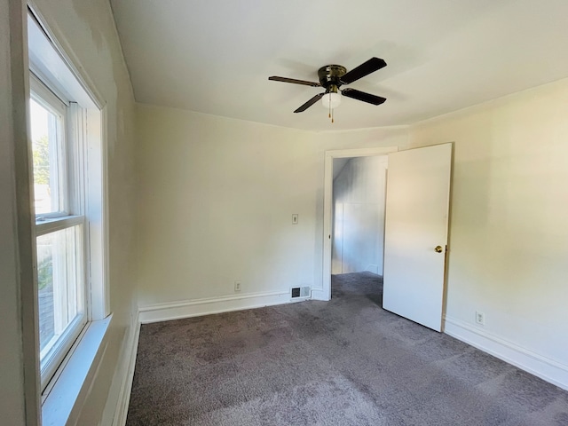 empty room with ceiling fan and dark colored carpet