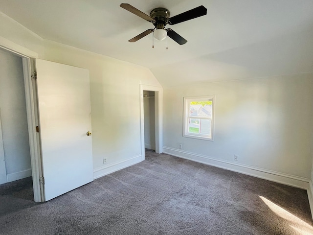 unfurnished bedroom with a walk in closet, lofted ceiling, dark carpet, and ceiling fan