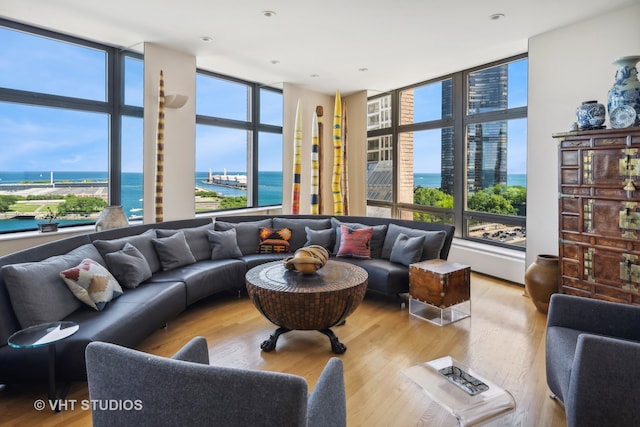 living room featuring a healthy amount of sunlight, a water view, light wood-type flooring, and a wall of windows