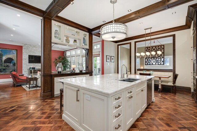 kitchen with white cabinets, hanging light fixtures, an island with sink, light stone countertops, and sink