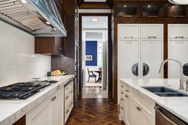 kitchen featuring wall chimney range hood, stainless steel appliances, dark parquet flooring, sink, and light stone countertops