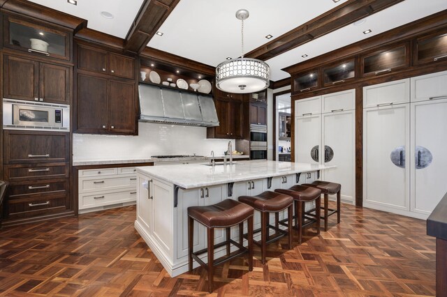 kitchen featuring an island with sink, hanging light fixtures, stainless steel appliances, dark parquet flooring, and white cabinetry