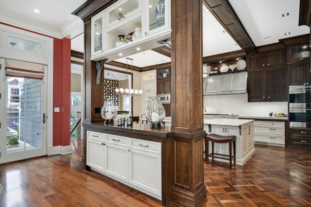 kitchen with dark brown cabinets, a kitchen breakfast bar, ornamental molding, double oven, and a center island