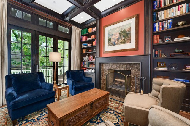 sitting room featuring coffered ceiling, a premium fireplace, beamed ceiling, and built in shelves