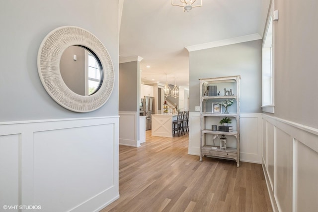 hall with light hardwood / wood-style floors, a healthy amount of sunlight, crown molding, and an inviting chandelier